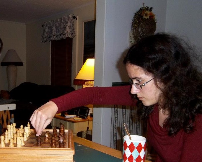 Picture is of author making a move in chess. Hair is messy, face is intense. She is very focused on the game. 