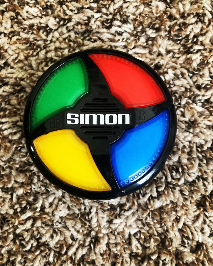 Game of Simon (round plastic toy with green, red, yellow, and blue buttons) on beige carpet